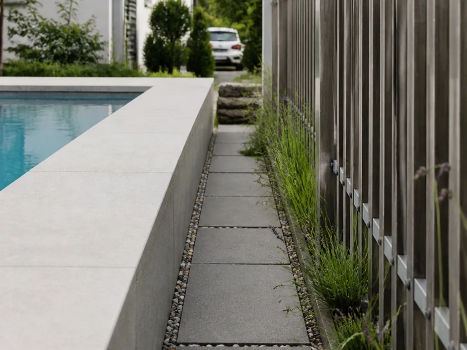 Schmaler Plattenweg zwischen Beckenkante und Gartenzaun