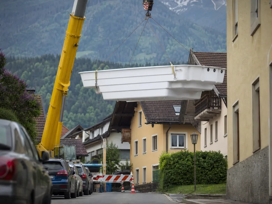 Mobilkran in einer engen Wohnstraße hebt ein Fertigbecken über eine Häuserzeile
